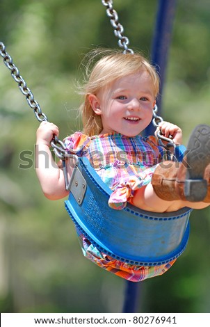 Three year old girl swinging high in a swing smiling.