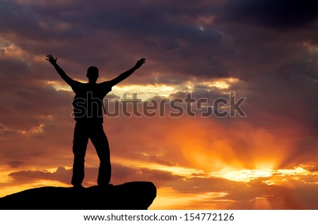 Silhouette of a man on a mountain top on sunset sky background