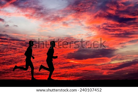 Silhouettes of two runners on sunset fiery background. Silhouettes of running mans against the colorful sky.