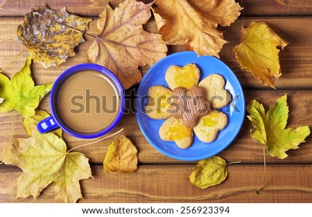 Cup of coffee and cookies on the table with dried autumn leaves. Drinking coffee in the fall on wooden table surrounded by dry leaves of autumn