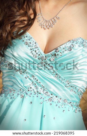 Upper torso of a young caucasian woman in a formal dance dress. She is wearing jewellery and has soft curls on her right