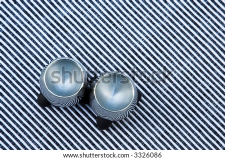 Two Steel egg cups on a black and white striped table cloth. Stripes of the cloth are at a diagonal and are reflected in the cups. The cups are empty.