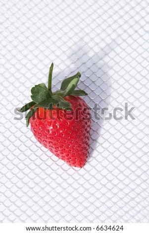 A fresh strawberry on a silver and white grid surface. The image is casting a shadow to the top right.  The image is shot in available light