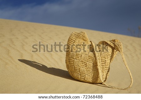 A woven beach bag lying on a sand dune. The sand is rippled from the tide and wind