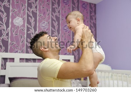 Father lifting little baby in home bedroom.