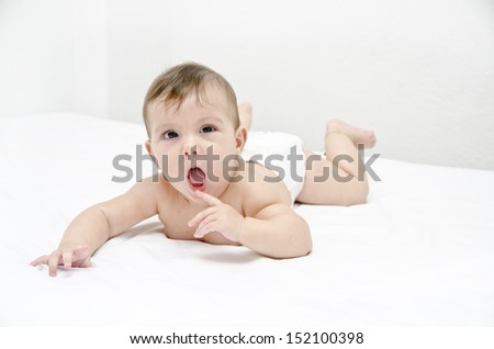 Baby biting finger in white bedroom.
