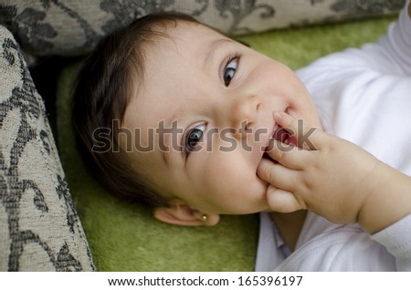 baby biting finger lying on home sofa