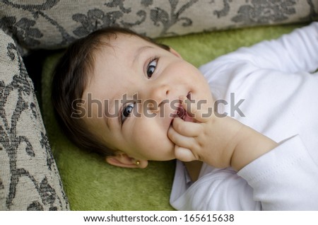 little baby biting fingers lying on home sofa