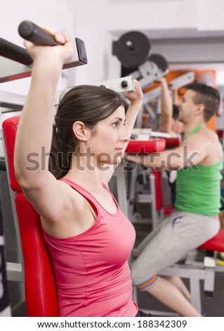 Man and woman training at gym machines, shoulder exercises