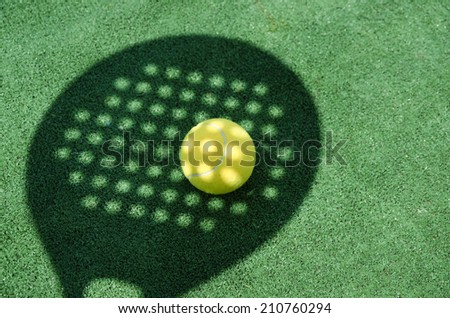 Paddle tennis racket shadow on ball in turf court