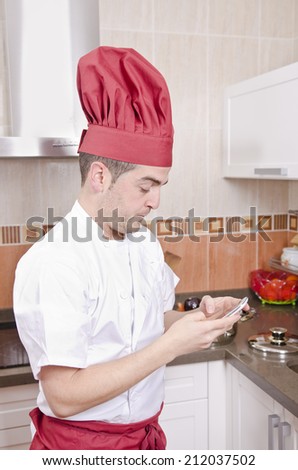 Chef touching smart phone in the kitchen with chef hat sending SMS or looking missing call.