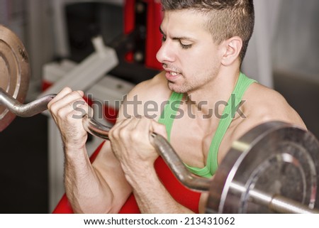Young man with weights bar training biceps in close up image at gym.