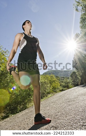Runner man warming legs with sun light flare effect in outdoors, warm up and stretching on road.
