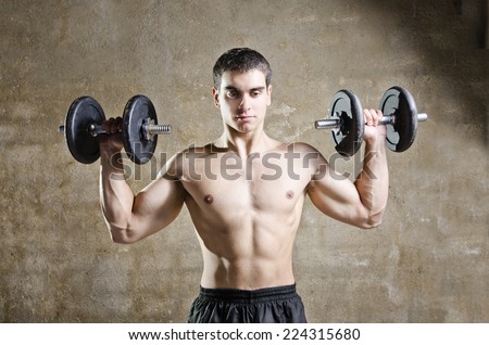 Young brunette man training shoulder muscles exercises in old gym