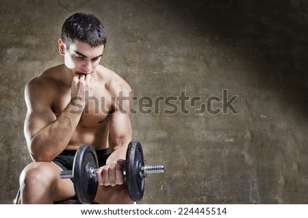 thoughtful and relaxed man training with dumbbell sit in old gym