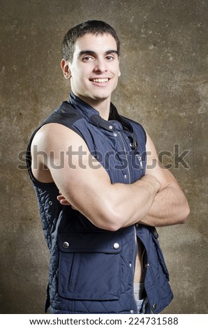 Posing strong young man with crossed arms on dirty wall background with sleeveless vest