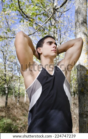 Runner man warming arms near to the trees, warm up and stretching