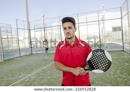 Team of paddle tennis in court. Image of man ready for serve and woman in background.