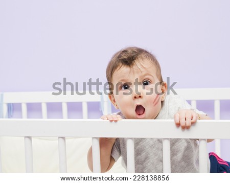 Fun baby with kiss mark on cradle in home bedroom.
