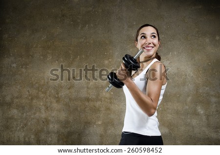 Young woman training biceps on dark concrete background