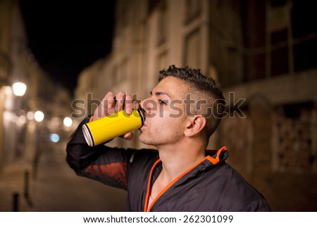 Young man drinking energy drink in the street with tracksuit resting and hydrating