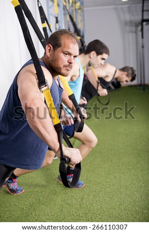 Group of three male people training at gym with elastic rope