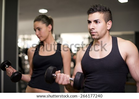 Couple lifting dmbbells weights training biceps at gym with ambient light