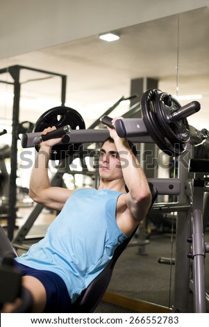 Young man lifting weights at gym training pectoral muscle.Natural light image.