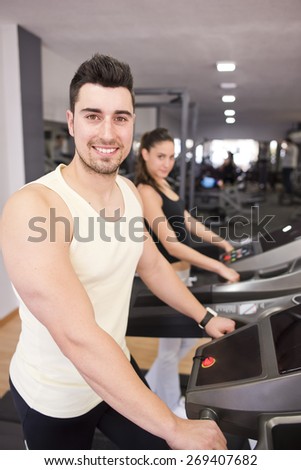 Young smiling man in treadmill ready for run. Woman in background