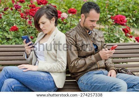 Couple in bench using telephone and writing in social networks or sms, phone addiction.
