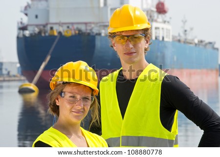 Male and female entrepreneurial engineers posing happily in front of a large industrial vessel