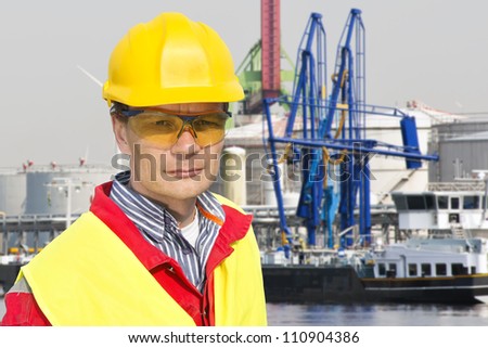 Portrait of a confident docker foreman in front of a petrochemical harbor with gas installations, numerous cranes, and a freight ship