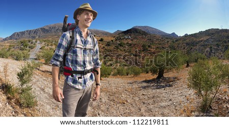 Hiker with a backpack on his back, on a hill, surrounded by a large olive grove, smiles broadly