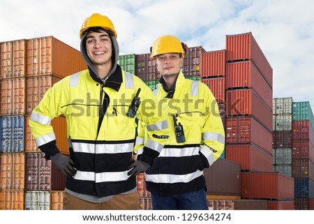 Two happy harbor workers posing in front of a huge stack of containers