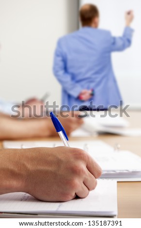 Man, taking notes in a classroom during workshop instructions, written by a teacher on a whiteboard