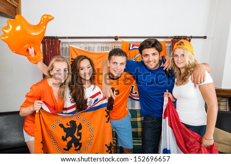 Portrait of happy multiethnic young Dutch soccer fans standing together at home
