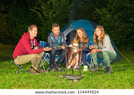 A group of friends sitting around a campfire in front of a tent