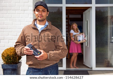 Delivery guy, holding a wireless pin machine walking away from a house, where a woman stands in the doorway, with the just delivered parcel in her hand