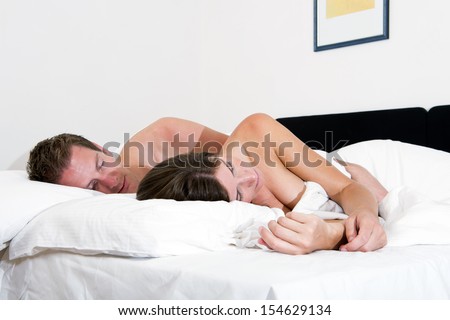Young couple sleeping in  late in a hotel bed, the man\'s hand wrapped around his girlfriends waist
