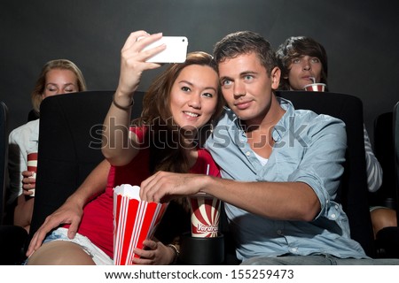 A young couple watching a movie at a cinema and photographing themselves with a Smartphone