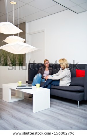 Two business women talking on a couch in a corporate waiting area before a sales pitch - creative industry