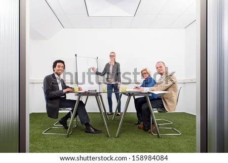 Small business meeting, with four people in a small stylish conference room with grass on the floor, discussing strategy, growth, sustainability and environmental inpact of business,