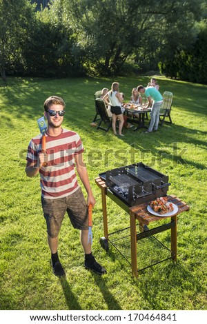 Confident Looking Man Standing With Kitchen Utencils In A Park With A Few Friends In The Background In The Late Summer Afternoon