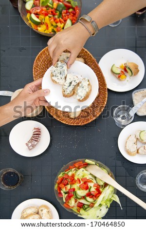 Summer Styled Dinner Table, With One Hand Passing A Plate With Bread And French Blue Cheese To Another Dinner Guest, Seen From Above