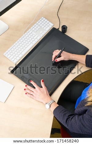 Woman with red finger nails working behind a grapic tablet, busy with computer aided design