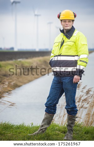 Project developer stands confident in a green landscape with his reflective jacket and safety helmet