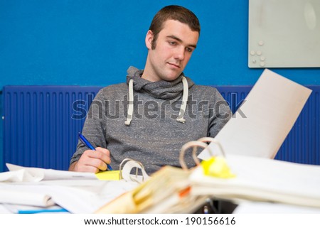 Young intern working at a messy desk, cluttered with folders, documents and paperwork