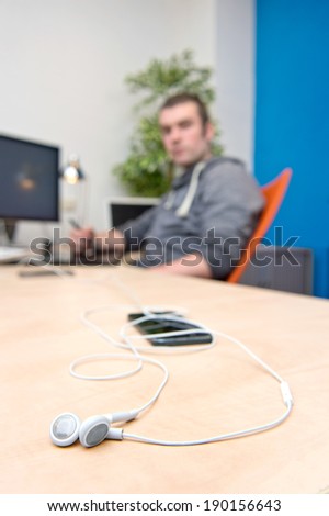 Ear phones, lying on a clean, paperless desk, with a man, working behind a computer in the background. A connectivity concept