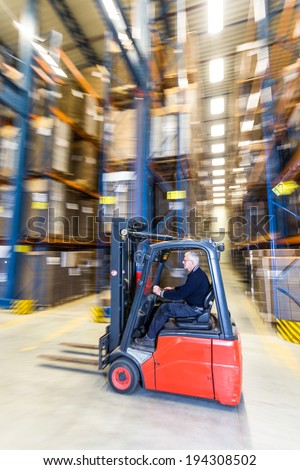 Reach truck forklift driving past an isle in a warehouse at speed. A panned image, with stock and cardboard boxes in the shelves of the storage racks. Conceptual image about internal logistics