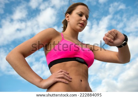 Fit, athletic woman wearing a sports bra and heart rate monitor checking her pulse during a training run